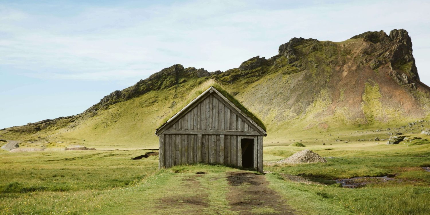 vikings An old wooden house stands alone in a vast green field under a clear blue sky.
